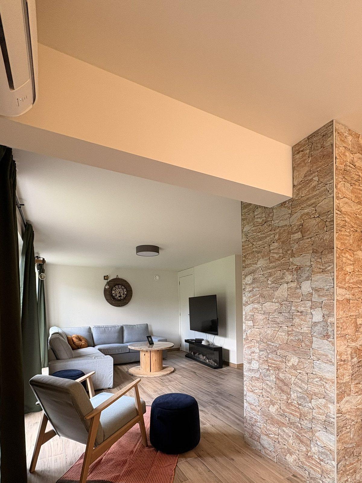 Zithoek met hoekzetel, fauteuil en smart-tv naast de natuurstenen muur, vakantiewoning in de Voerstreek