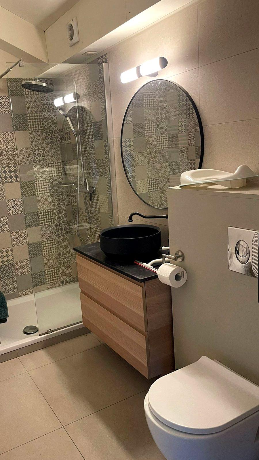 Badkamer met inloopdouche, ronde spiegel en zwarte waskom in vakantiewoning Teuven