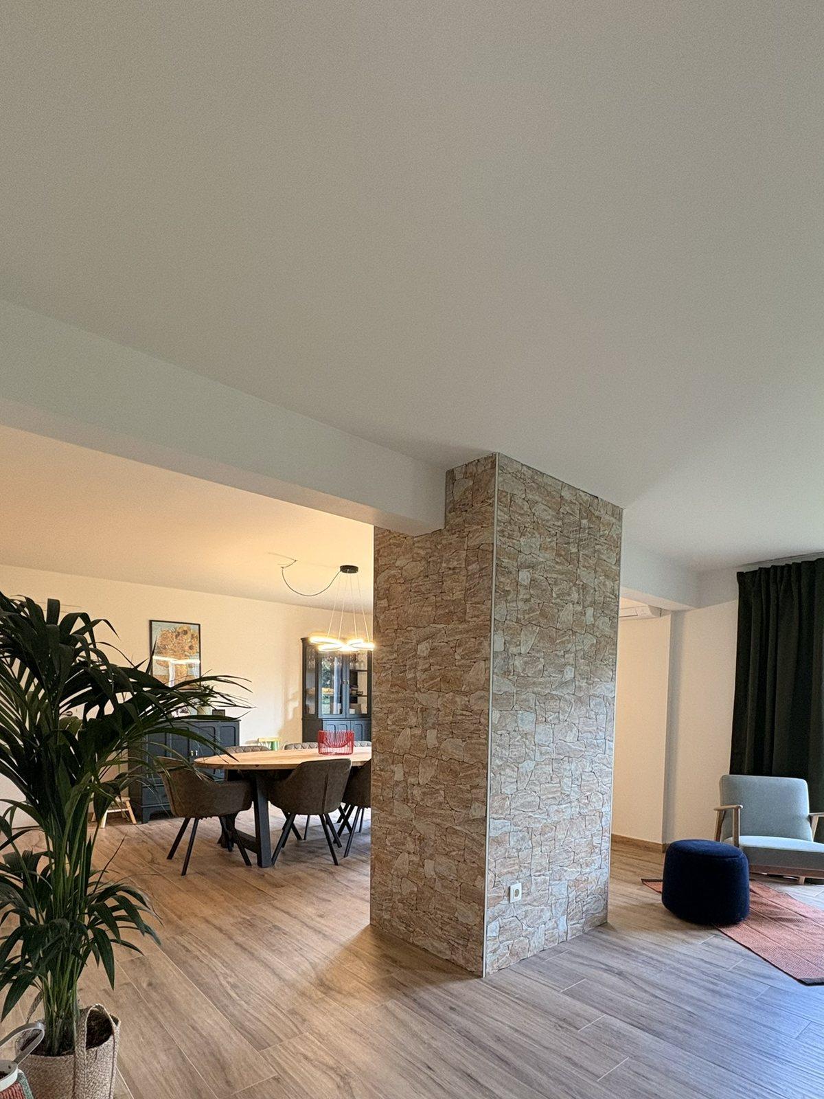 Doorkijk langs de natuurstenen muur naar de eettafel en de zithoek, Maison Campagnard in Teuven
