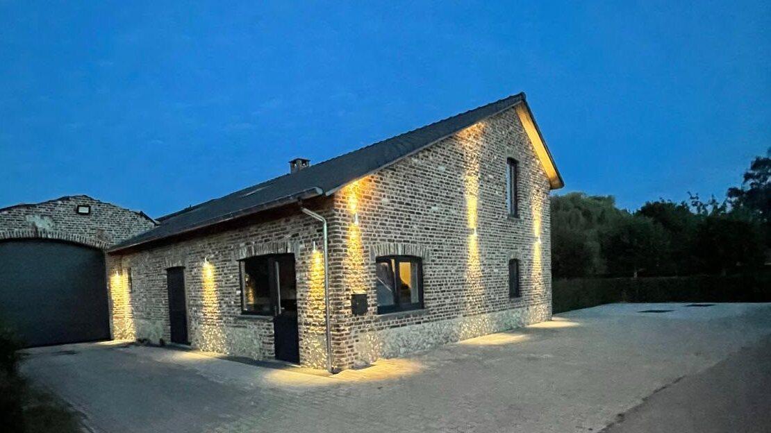 Maison de vacances Maison Campagnard à Teuven à la tombée du jour, avec un éclairage chaleureux le long de la façade en briques