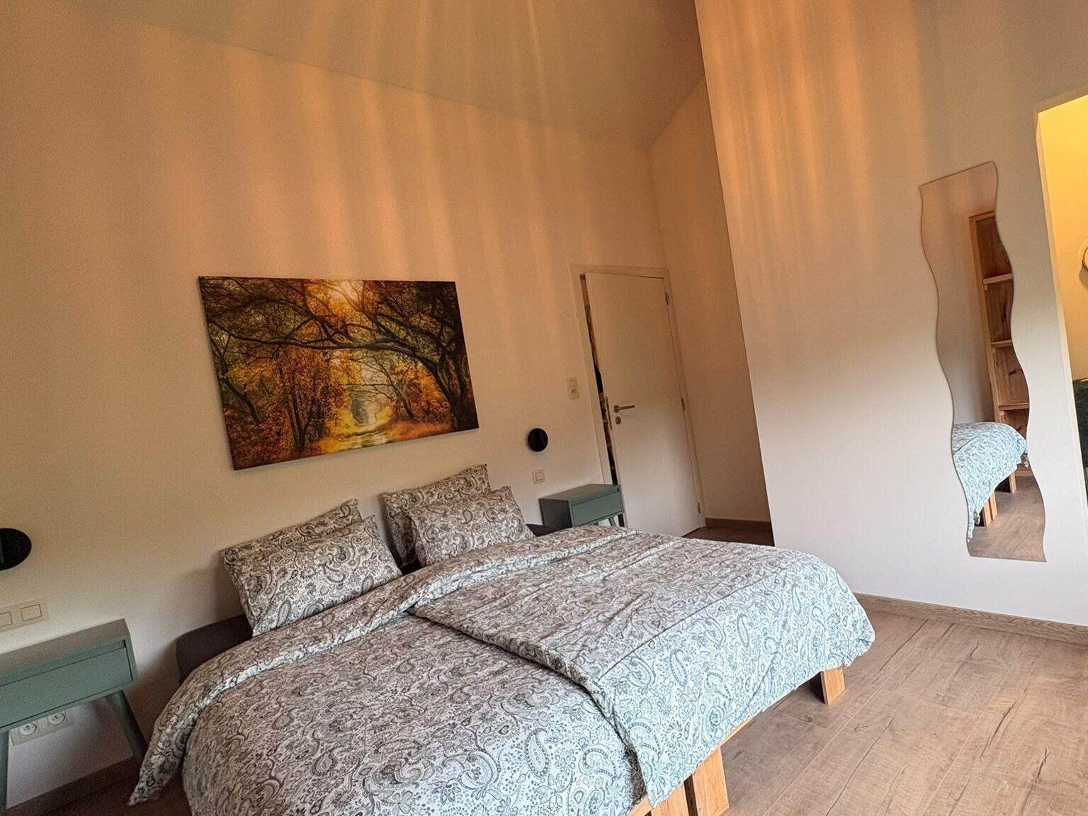 Chambre à l'étage avec lit double, tableau d'une forêt d'automne et vue sur la douche et le lavabo privés, maison de vacances Maison Campagnard à Teuven