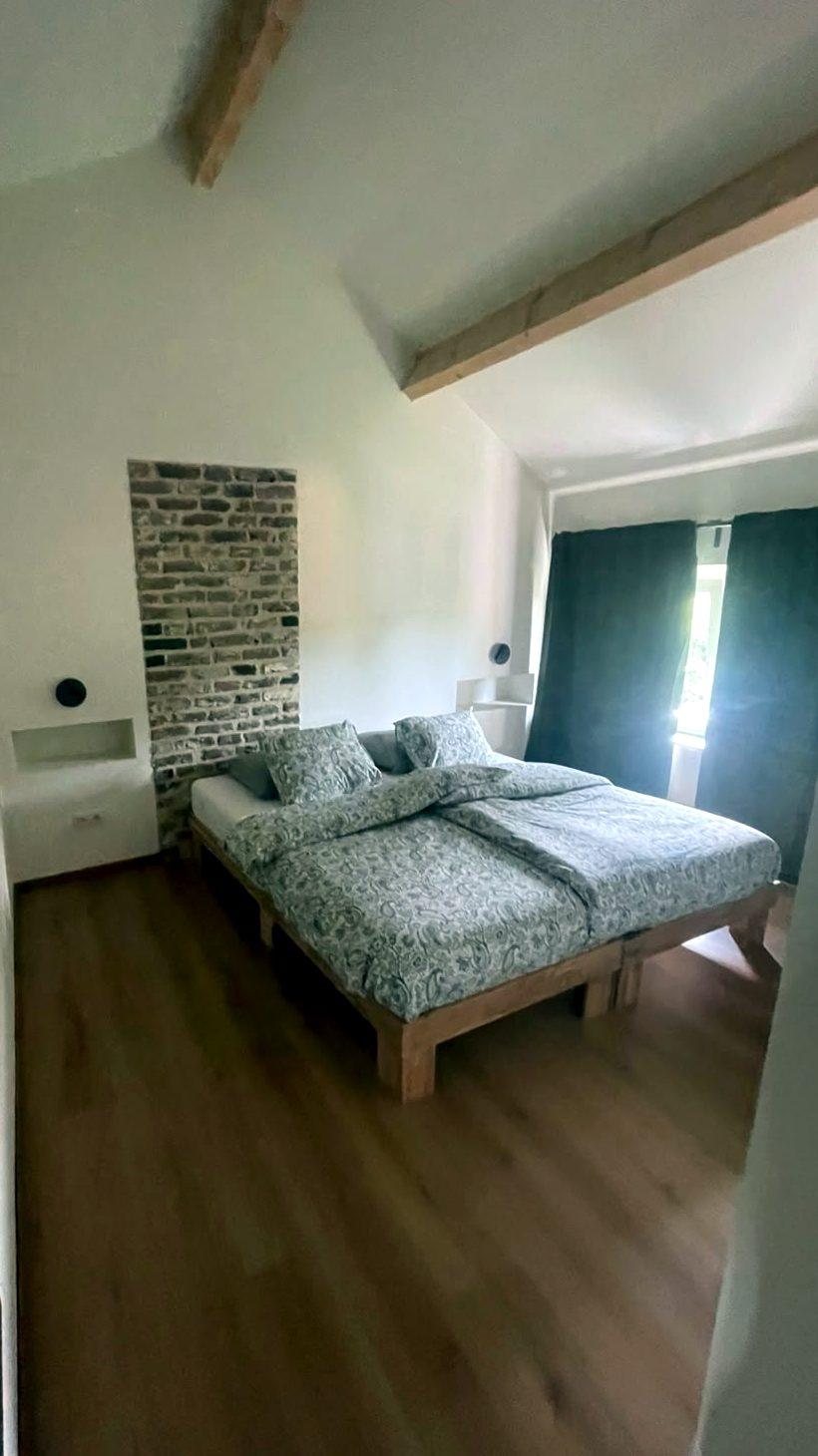 Slaapkamer boven met bewaarde bakstenen muur, vakantiewoning Maison Campagnard in Teuven