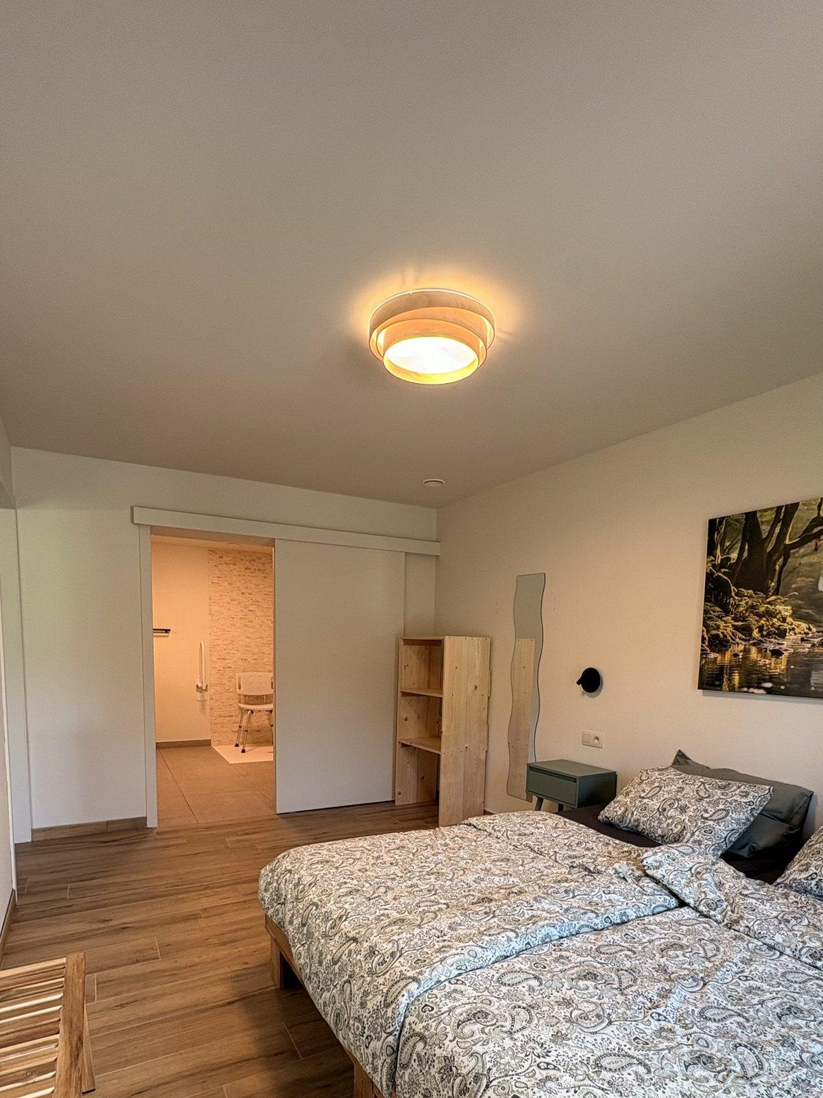 Gelijkvloerse slaapkamer met tweepersoonsbed en schuifdeur naar de eigen aangepaste badkamer, vakantiewoning Maison Campagnard in Teuven